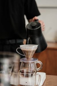 Barista zalewający dripa gorącą wodą z czajnika o wąskiej szyjce, ilustrujący metody alternatywne parzenia kawy w trzeciej fali kawy.