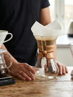 Trzy popularne alternatywne metody parzenia kawy: biały drip Hario V60 na serwerze, szklany Chemex z filtrem oraz Clever Dripper na drewnianym stole.