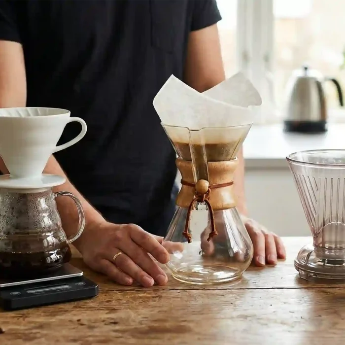 Trzy popularne alternatywne metody parzenia kawy: biały drip Hario V60 na serwerze, szklany Chemex z filtrem oraz Clever Dripper na drewnianym stole.