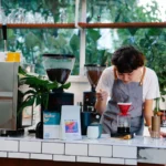 Młoda kobieta-barista w fartuchu przygotowuje kawę rzemieślniczą metodą przelewową (dripper) na wagdze w kawiarni.