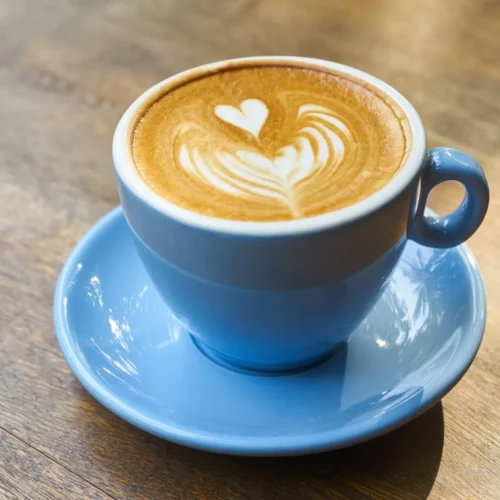 Cappuccino z rozetą latte art w niebieskiej filiżance na drewnianym stole