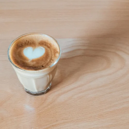 Cortado w małej szklance z sercem z mlecznej pianki na drewnianym blacie