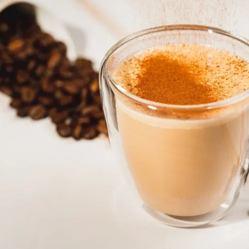 Domowe pumpkin spice latte w szklanym kubku posypane cynamonem, obok ziarna kawy